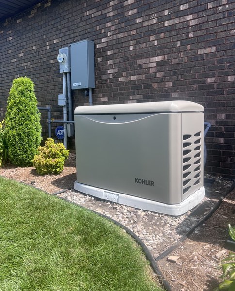 Kohler standby generator on an AGS-stamped pad beside a brick home