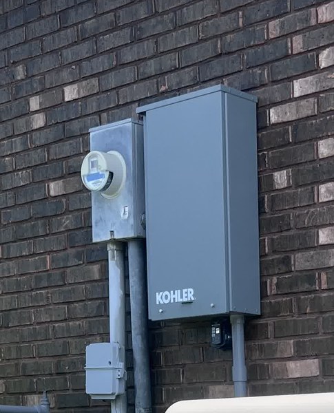 Kohler automatic transfer switch and meter socket mounted on a brick wall as part of an AGS installation